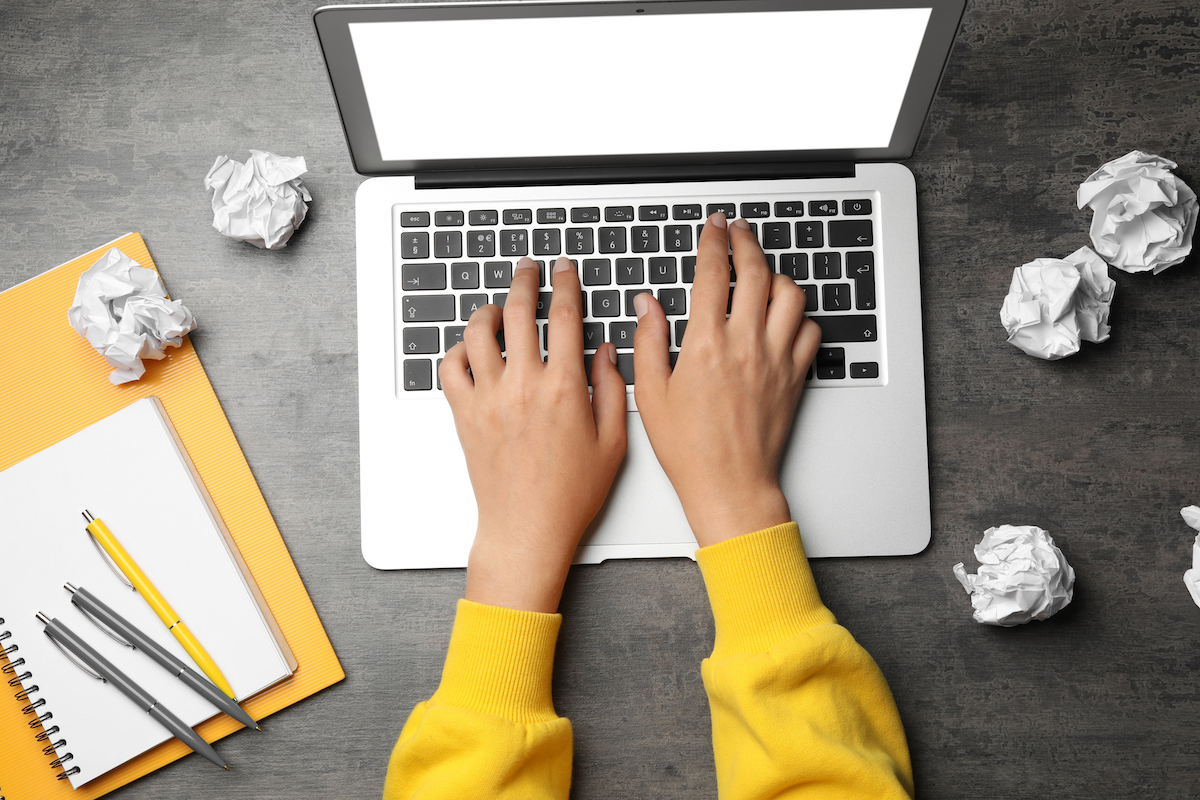 Woman using laptop at table with crumpled paper