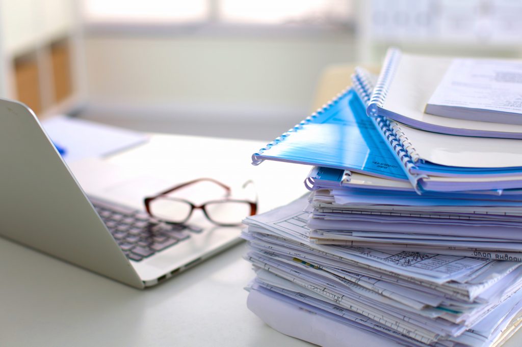 Laptop with stack of folders on table on white background